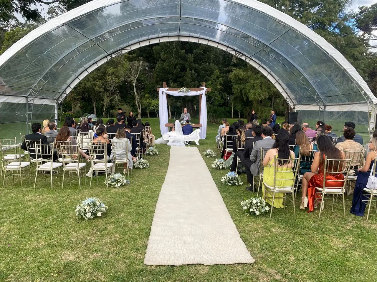 Ceremonia bajo carpa transparente con invitados y altar blanco