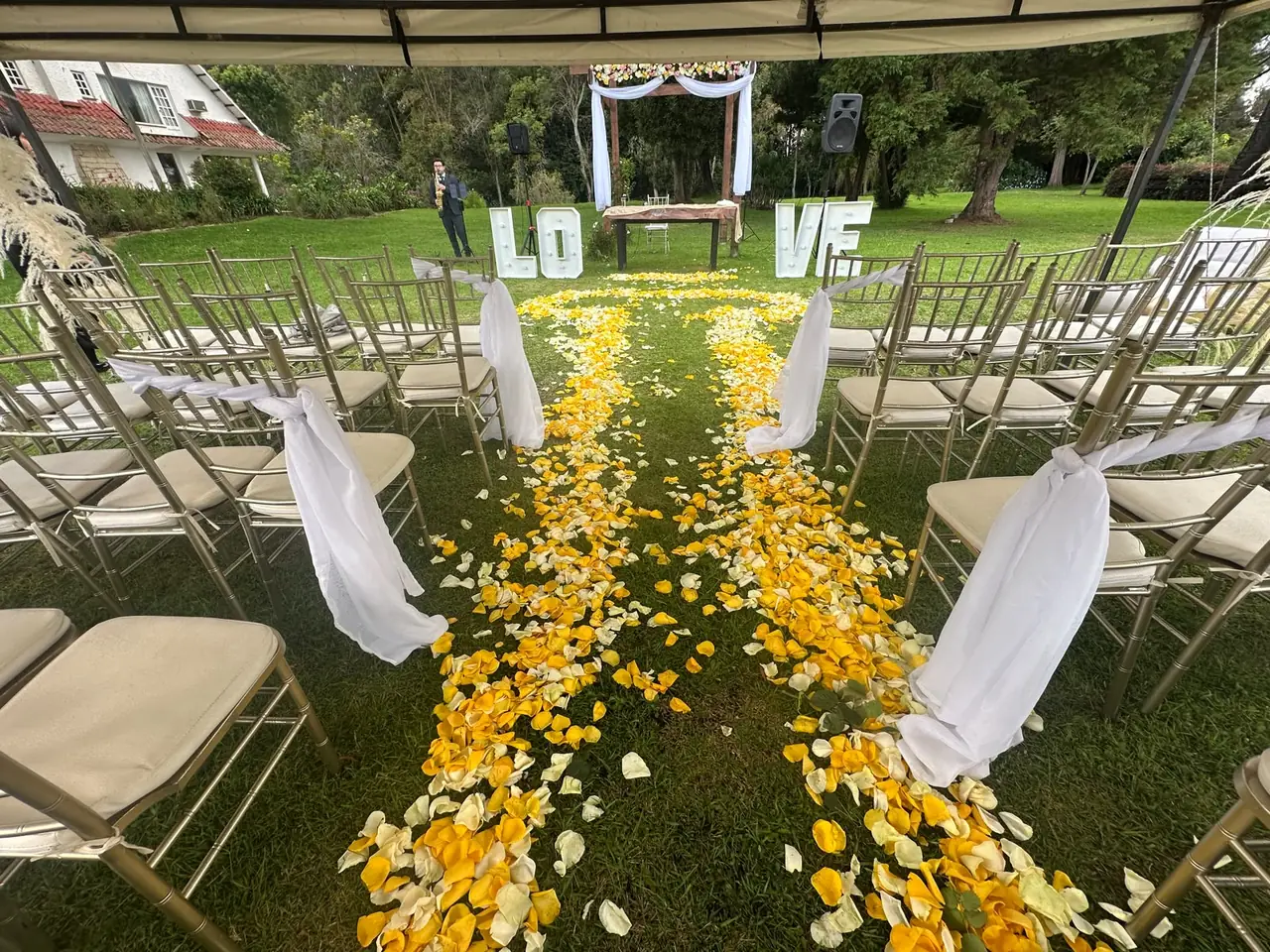 Ceremonia en jardín con pasillo de pétalos, telas blancas y letras LOVE
