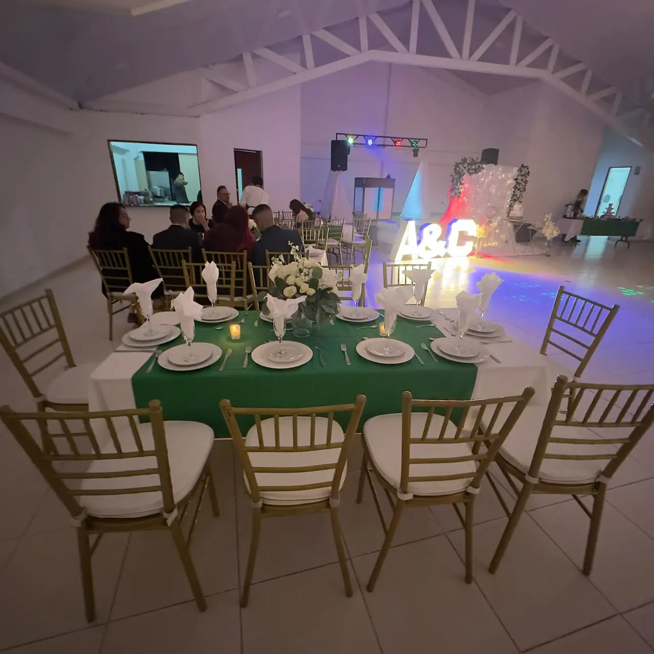 Recepción íntima con mesas vestidas en verde y letras iluminadas
